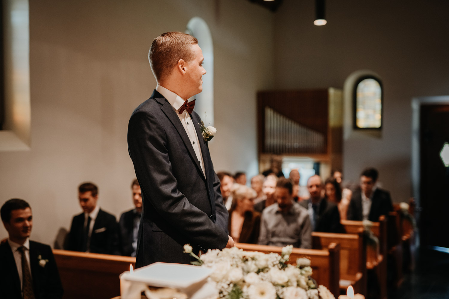 Hochzeitsfotograf in der Marienkapelle in Morschach Schweiz Hochzeitsfotografin kirchliche Trauung Schweizer Berge Alpen natürliche Hochzeitsfotografie Bräutigam wartet auf Braut