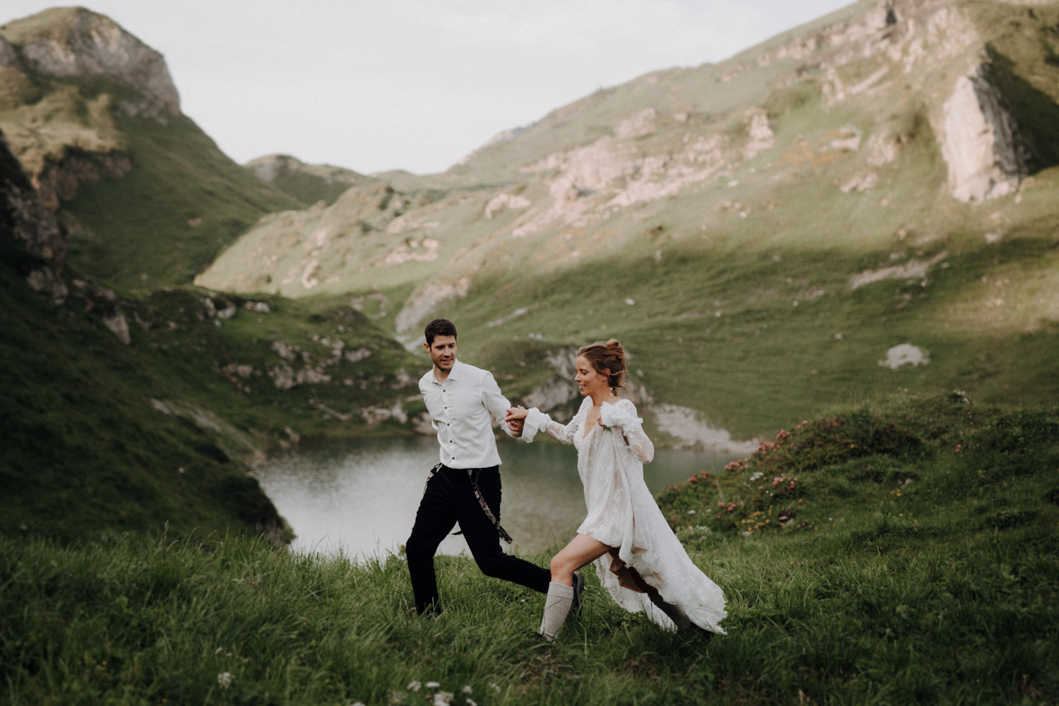Brautpaar rennt über eine Wiese an einem Bergsee in den Bergen Schweizer Alpen